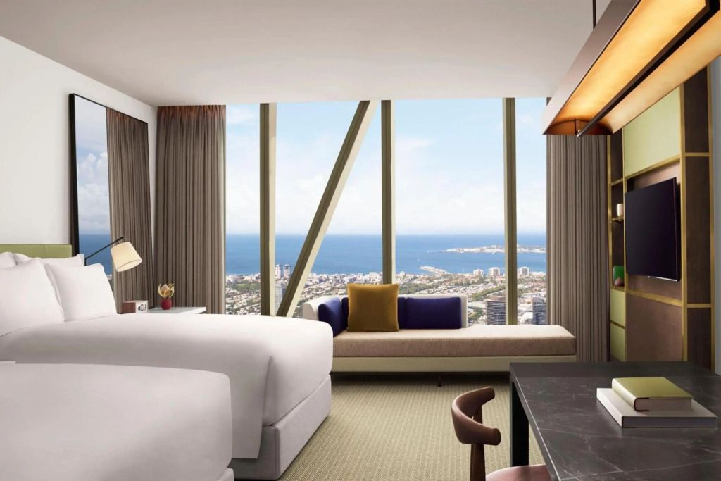 Modernes Hotelzimmer mit Panoramablick auf Stadt und Ozean durch große Fenster.