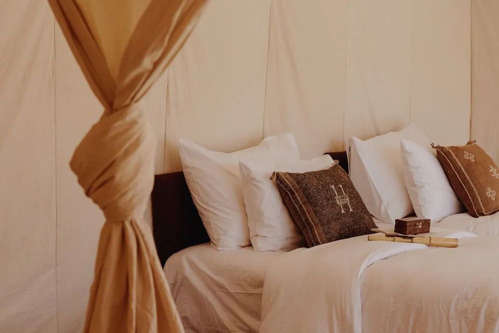 Gemütliches Bett mit Kissen und rustikaler Dekoration im Umnya Dune Camp.