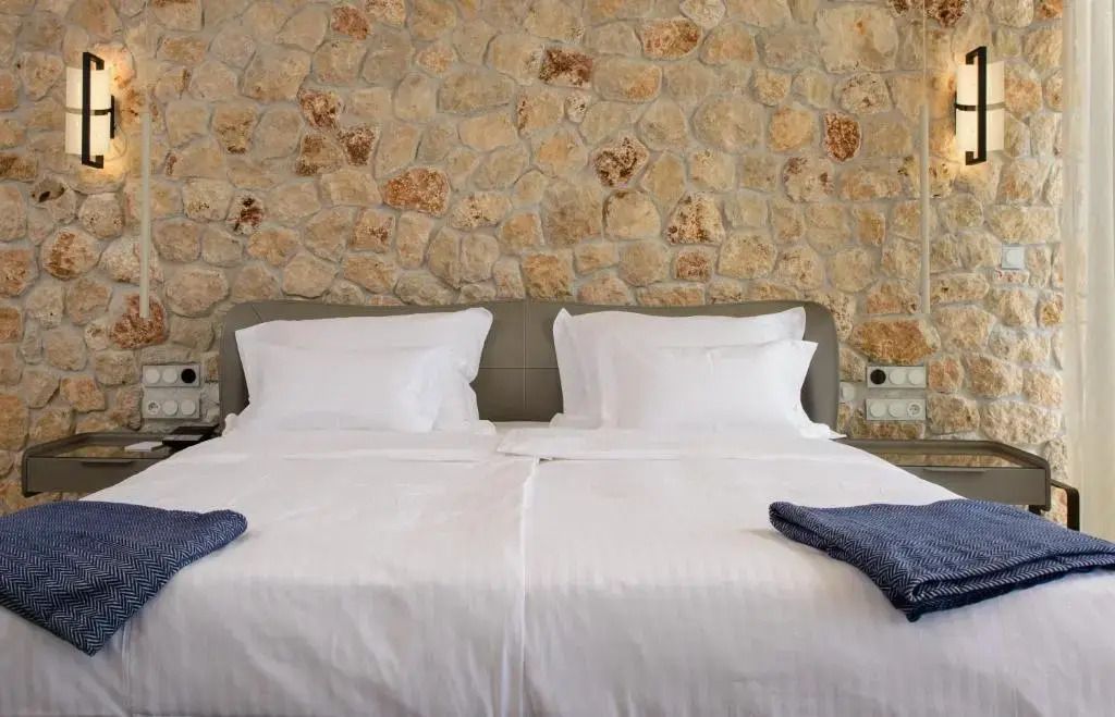 Elegantes Doppelbett vor Natursteinwand mit weißer Bettwäsche