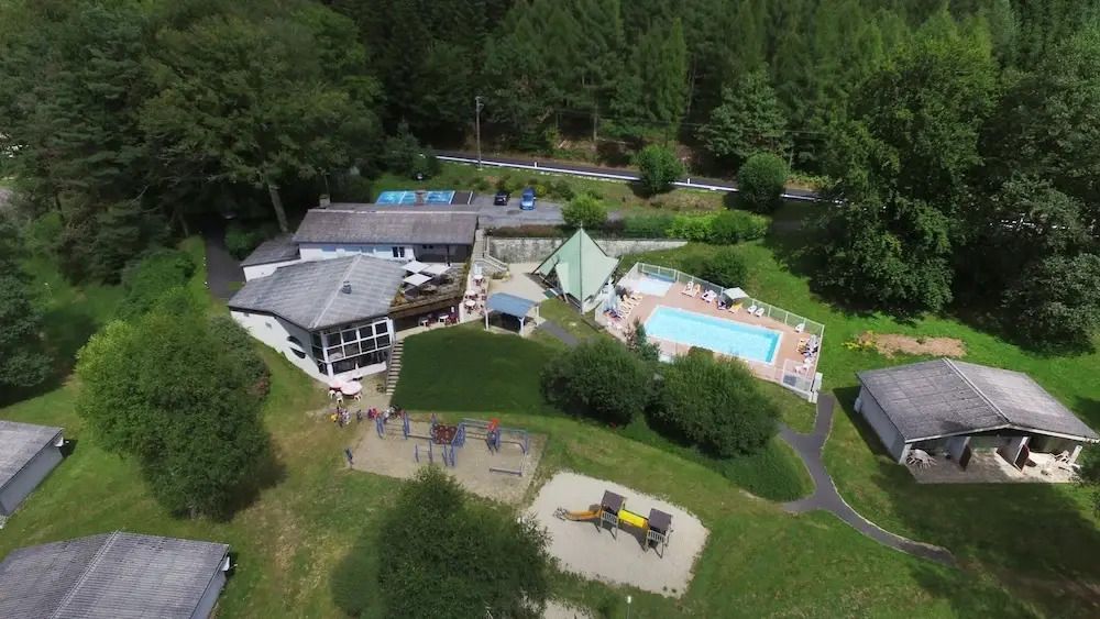 Luftaufnahme von Hotelanlage mit Pool und Spielplatz in grüner Umgebung
