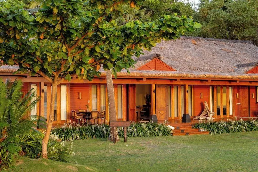 Luxusvilla mit Strohdach in tropischer Gartenanlage bei Sonnenuntergang.