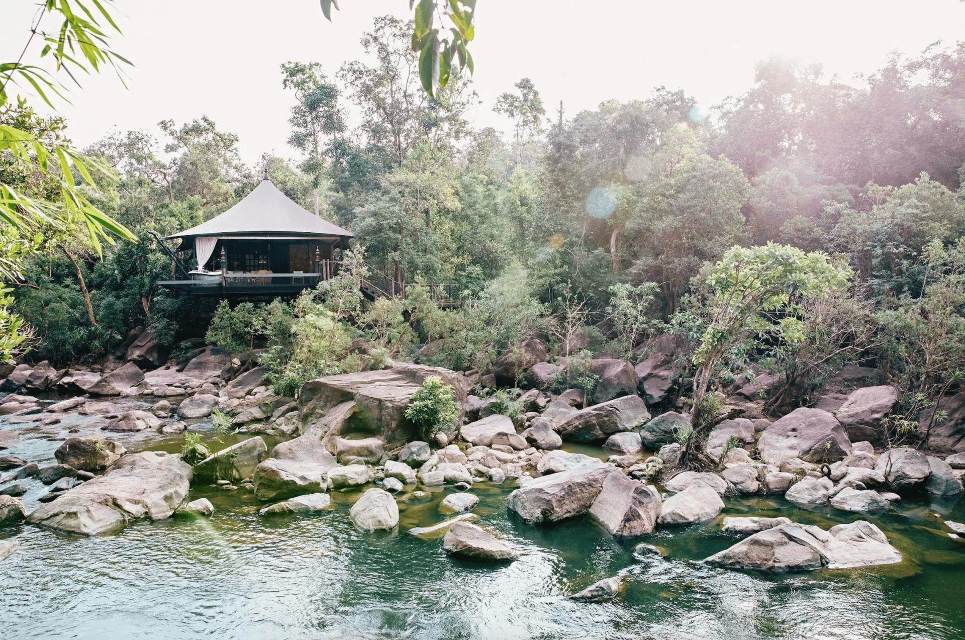 Luxus-Safarizelt am Flussufer umgeben von dichtem Wald und großen Felsen