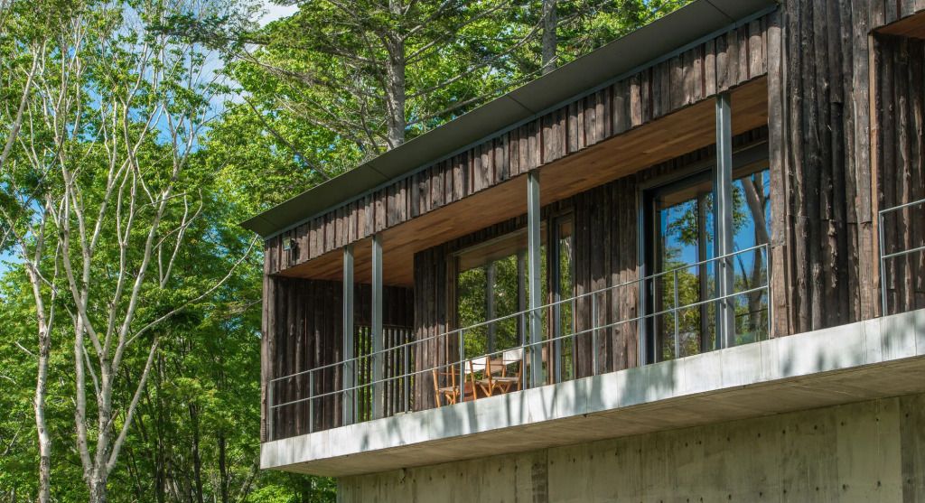 Moderne Holzwand-Architektur mit großen Fenstern und Balkon im Grünen.